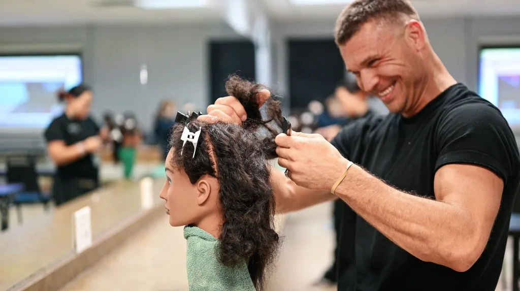 Male cosmetology student works on haircuts in the classrom